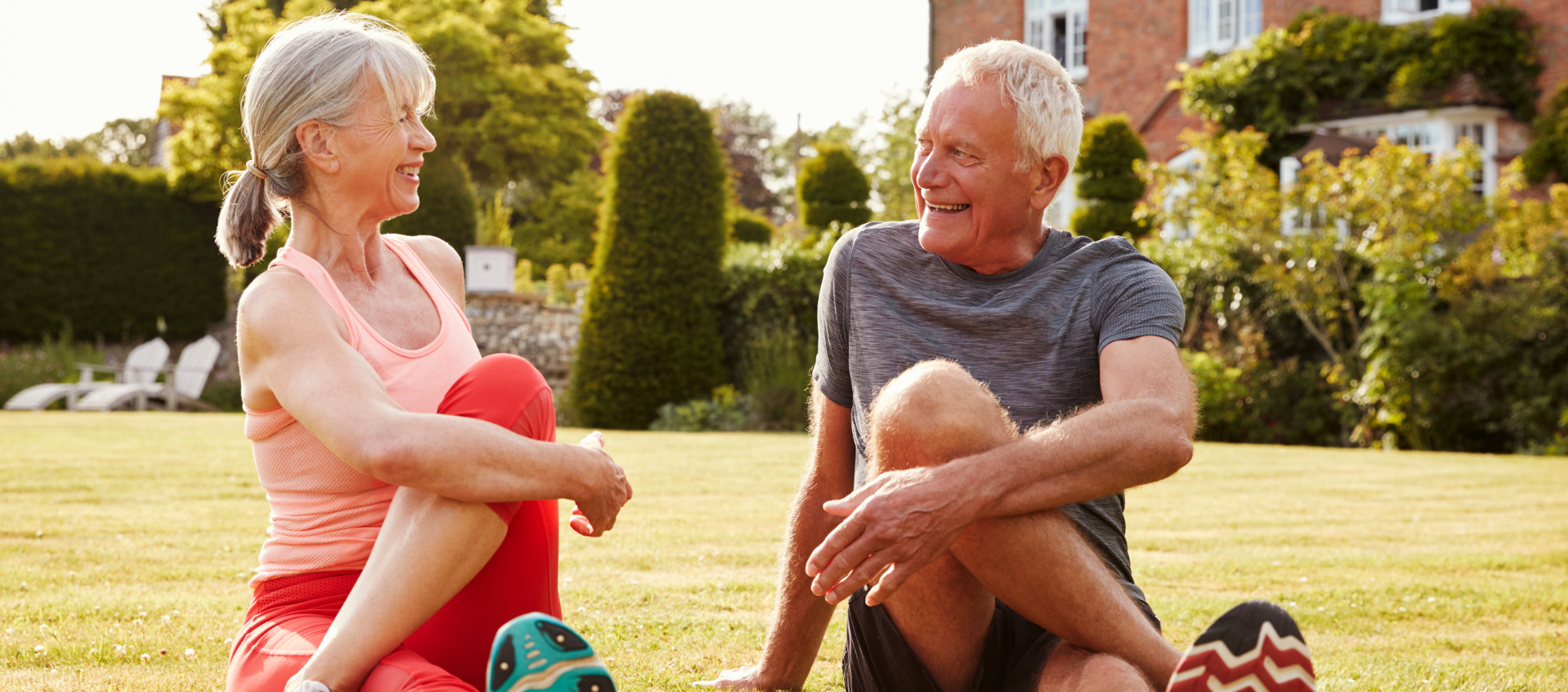 Older man and woman, seated stretching in a park