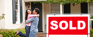 Couple in front of home with sold sign