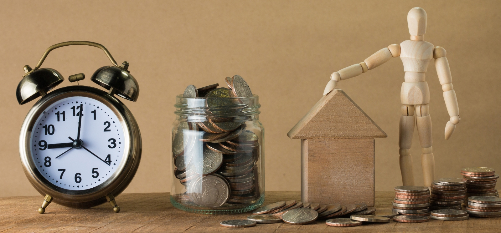 Alarm clock, jar of change, small wooden house, and small wooden man all surrounded by loose change