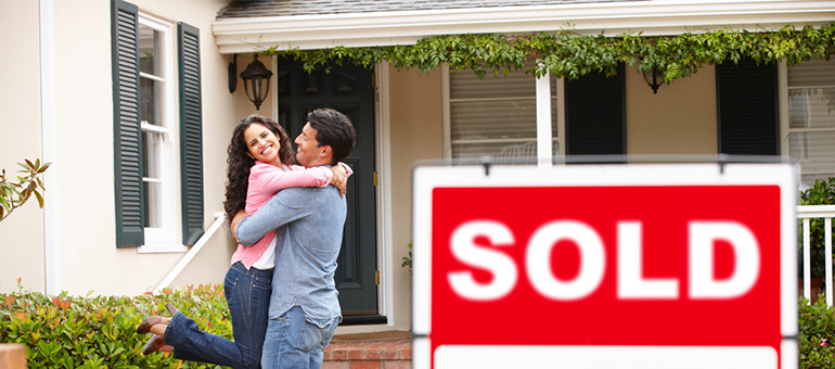 Couple in front of home with sold sign