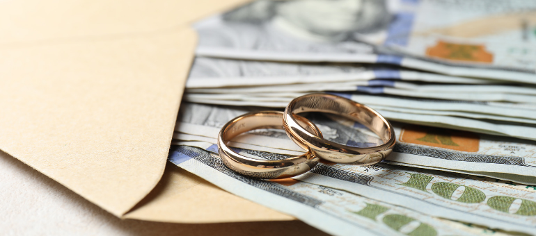 Money sticking out of an envelope with two gold wedding bands laying on top
