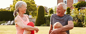 Older man and woman, seated stretching in a park