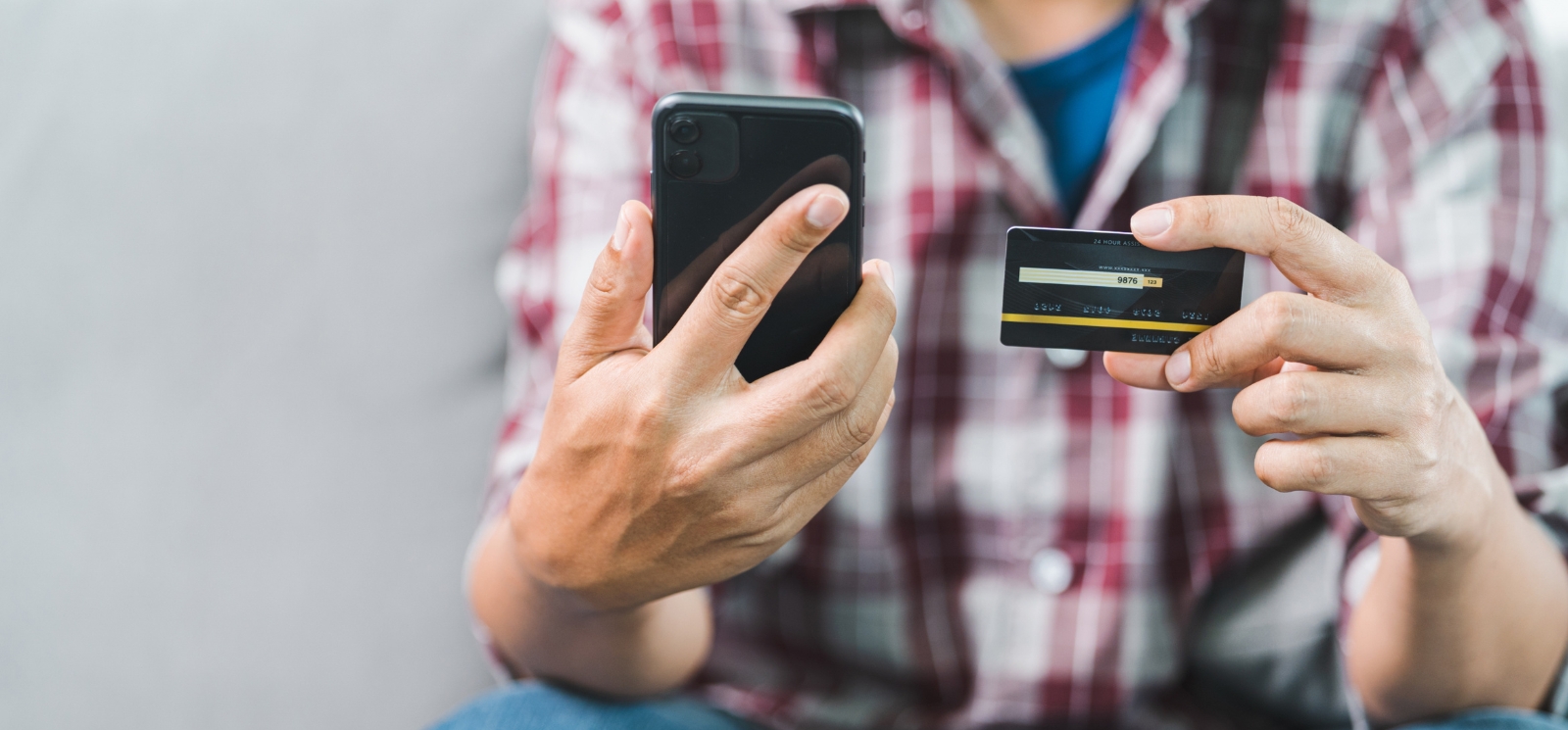 Up close photo of man in a plaid shirt holding a phone and a debit card
