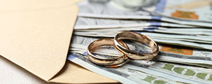 Money sticking out of an envelope with two gold wedding bands laying on top